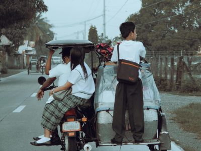 Group of children in school uniforms riding a tricycle on a street in the Philippines.