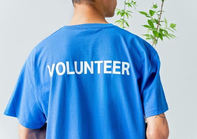 A person in a blue volunteer shirt stands in front of a plant.